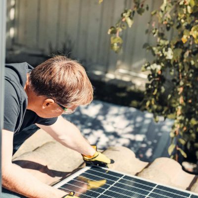 An adult male installing a solar panel on a rooftop, highlighting clean energy technology.